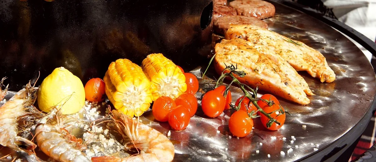 Креветки, лимон, кукуруза, томаты черри и курица на жарочной поверхности из пищевой нержавеющей стали